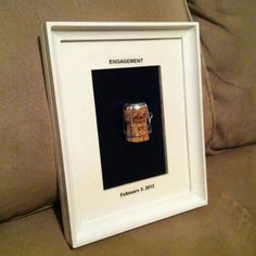 a framed photograph of a beer can with the word engagement printed on it, sitting on a couch