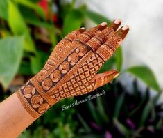 a woman's hand with henna tattoos on it and green leaves in the background