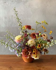 a vase filled with lots of colorful flowers on top of a wooden table next to a wall