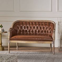 a brown leather couch sitting on top of a wooden floor next to a vase filled with flowers