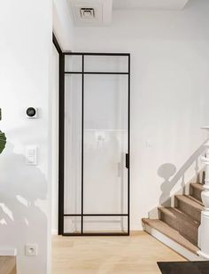 a white room with stairs and a glass door leading to the second floor, next to a potted plant