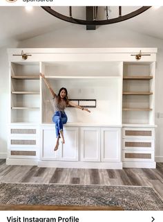 a woman standing on top of a white book shelf in a living room under a chandelier