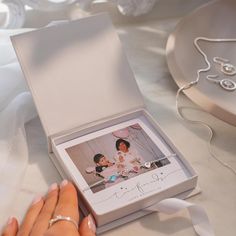 a woman's hand holding a ring in front of an open box with a photo on it