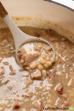 a wooden spoon in a pot filled with beans and ham