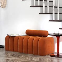 an orange couch sitting in front of a stair case next to a table with a magazine on it