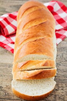 a long loaf of bread sitting on top of a wooden table next to a red and white checkered napkin