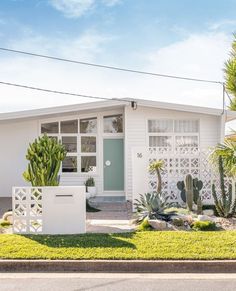 a small white house with cactus and cacti in the front yard on a sunny day