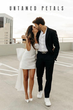 a man and woman are kissing in an empty parking lot with buildings in the background