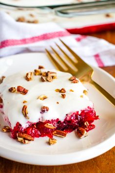 a white plate topped with a piece of cake covered in frosting and pecans