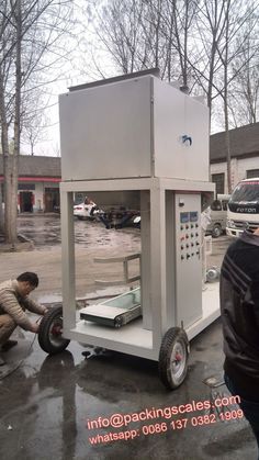 two men are working on a machine in the parking lot with another man nearby looking at it