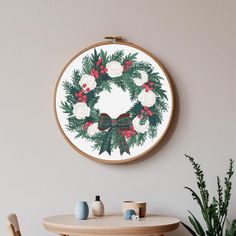 a cross stitch christmas wreath hanging on the wall next to a table with two chairs