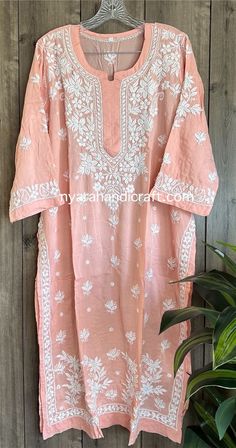 an embroidered pink top hanging on a wooden wall next to a potted green plant