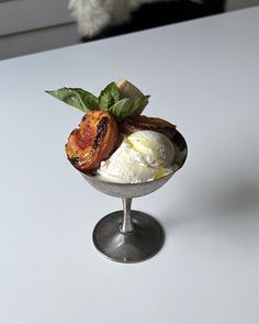 an ice cream sundae with bacon, peaches and mint on a white table