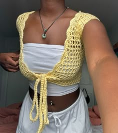 a woman wearing a yellow crochet top and white shorts with a necklace on her neck