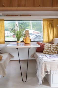 a room with two beds and a table in front of the window that has yellow drapes