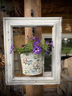 a white frame with purple flowers hanging from it's side on a wooden wall