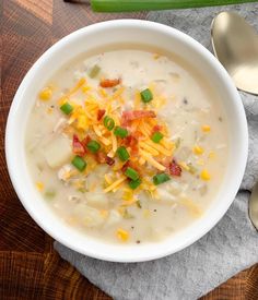 a white bowl filled with soup and cheese on top of a wooden table next to spoons