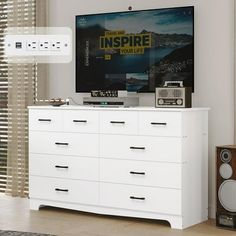 a white dresser with speakers and a television on it in front of a large window