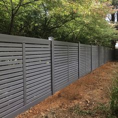 a fence that is next to some trees and dirt on the ground in front of it