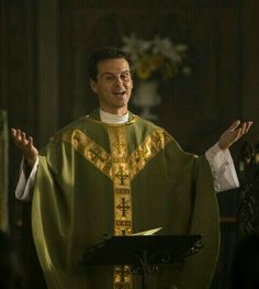 a man in a priest's outfit standing at a podium with his hands out