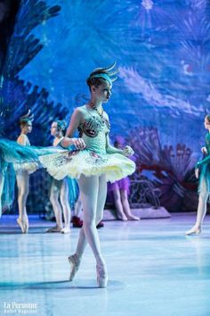 the young ballerina is dressed in green and gold with feathers on her head as she performs