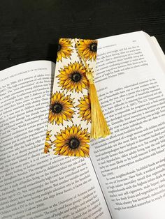 an open book with a tassel on top of it next to a pair of sunflowers