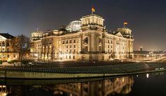 the building is lit up at night with its lights on and reflecting in the water