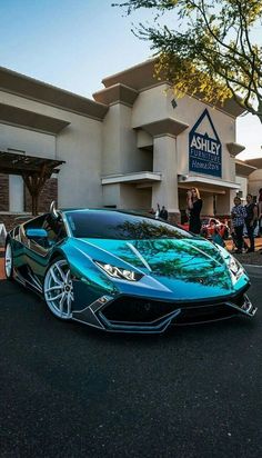 a blue sports car parked in front of a building with people standing around it on the sidewalk