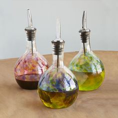 three glass bottles with different colored liquids in them sitting on a wooden table next to each other