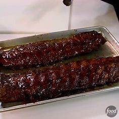 two pieces of meat sitting on top of a metal pan covered in bbq sauce