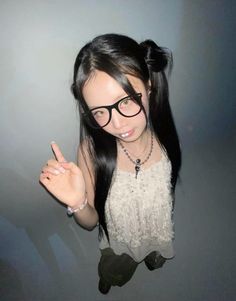 a woman wearing glasses making the peace sign with her hand while standing in front of a gray wall