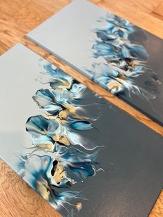 two blue and white paintings on wood flooring next to each other, one with flowers in it