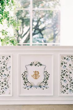 two framed pictures on the wall in front of a window with white flowers and greenery