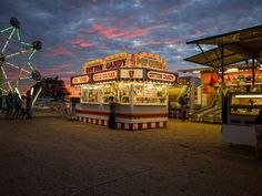 an amusement park at dusk with ferris wheel and food stand in the foreground,