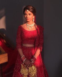 a woman in a red dress and gold jewelry standing next to a piano with her hands on her hips