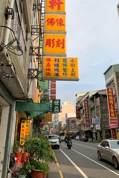 a city street with cars parked on both sides and chinese signs hanging from the side of buildings