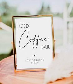 a sign that says iced coffee bar sitting on top of a wooden table next to a white feather