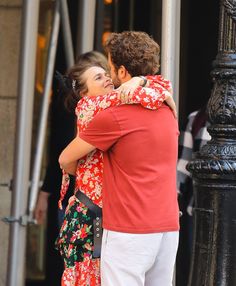 a man and woman embracing each other in front of a black pole on the street