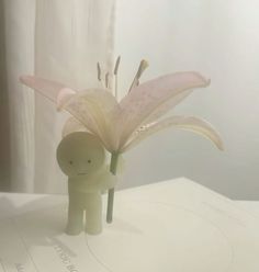 a small figurine holding a pink flower on top of a white tablecloth