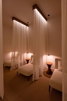 a room with three beds and two lamps on either side of the bed are white drapes hanging from the ceiling