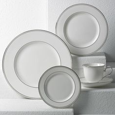 three white plates and two cups sitting on top of a shelf next to each other