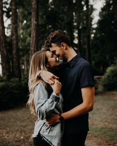 a man and woman standing in front of some trees with their noses to each other