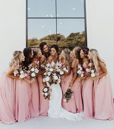 a group of women standing next to each other in front of a window holding bouquets