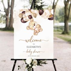 a welcome sign for a baby shower with teddy bears and balloons on it in front of some trees