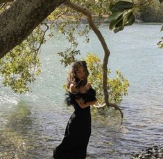 a woman is standing in the water with her arms around her neck and wearing a black dress