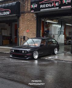 a black car parked in front of a redline auto shop on a rainy day