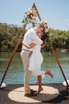 a bride and groom kissing in front of a lake with flowers on it's head