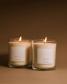 two candles sitting next to each other on top of a brown surface with one candle lit