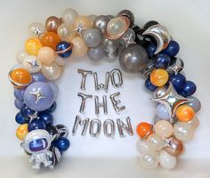 a wreath made out of balloons with the words two the moon written in silver and orange