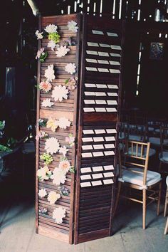 a tall wooden display with flowers on it's sides and chairs in the background